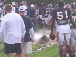 Denver Broncos Coach Josh McDaniels (left) and Lee Robinson (51, right) watch rookies participate in a muddy fumble recovery drill during the team's Wednesday afternoon practice.  The rookies were hosed while having to leap into the mud in attempts to recover a fumble.  (BroncoTalk/Kyle Montgomery)